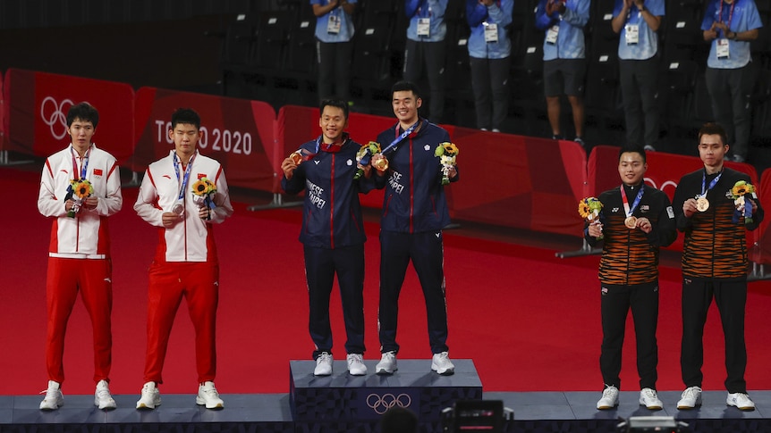 The badminton teams stand on the podiums with their medals. 