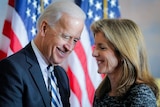 Joe Biden and Caroline Kennedy grinning at each other in front of a US flag. 