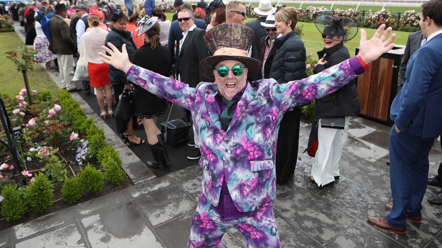 Steve Hopes raises his arms while wearing a multi-coloured suit at the Melbourne Cup.