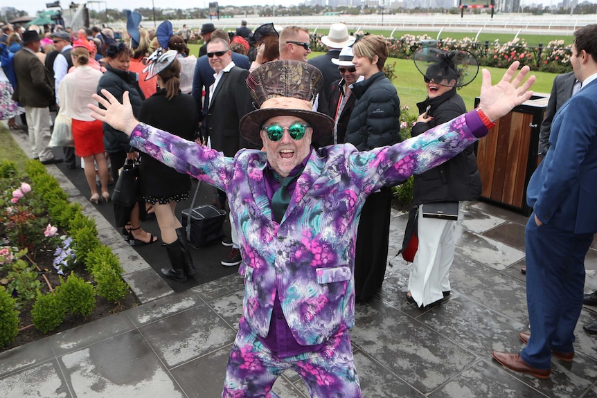 Steve Hopes raises his arms while wearing a multi-coloured suit at the Melbourne Cup.