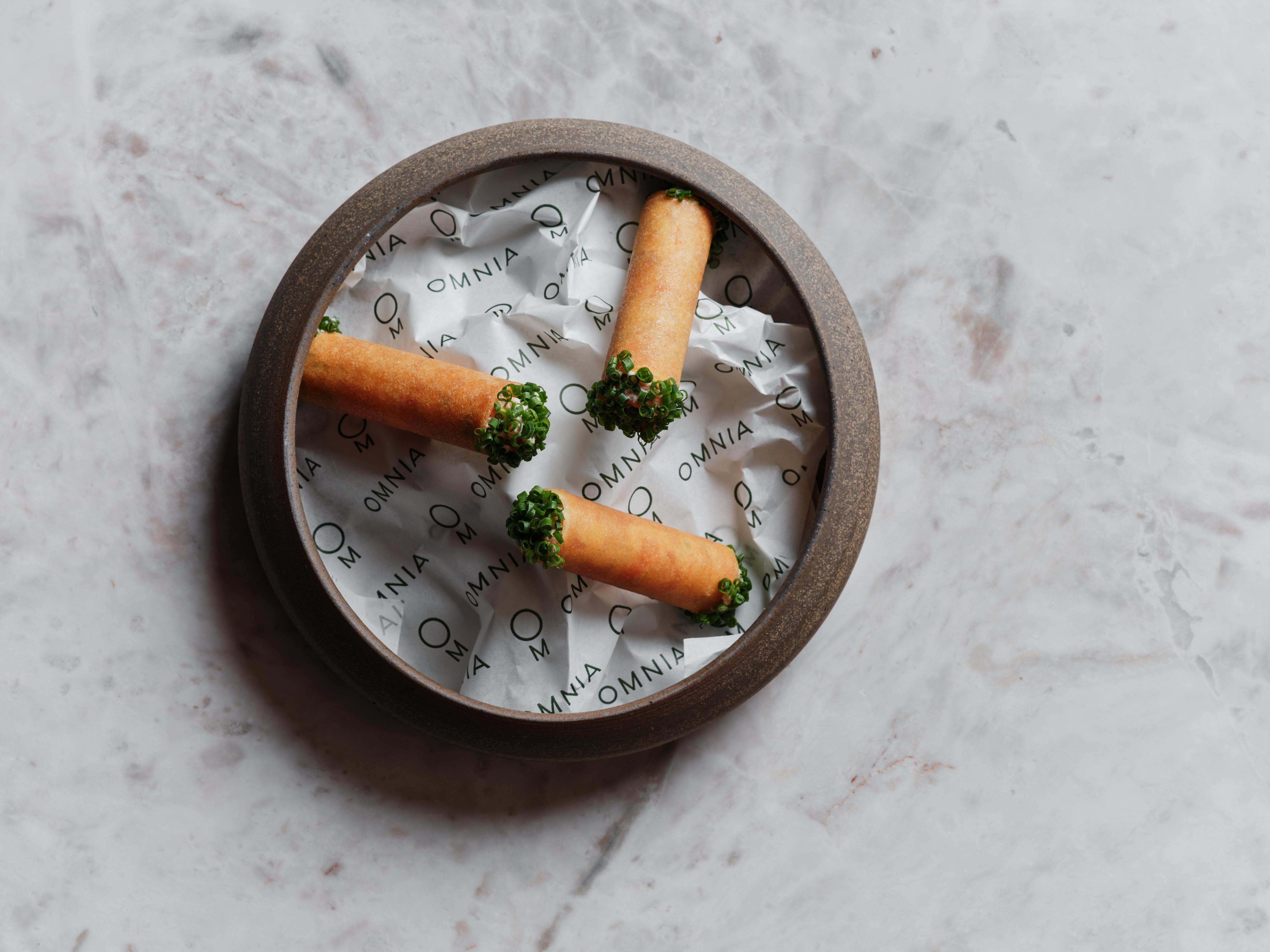 A plate of three pastry tubes with green chives on the ends.