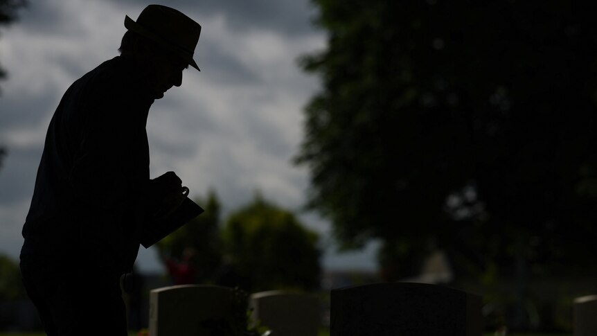 A silhouette of a man stands over a grave 