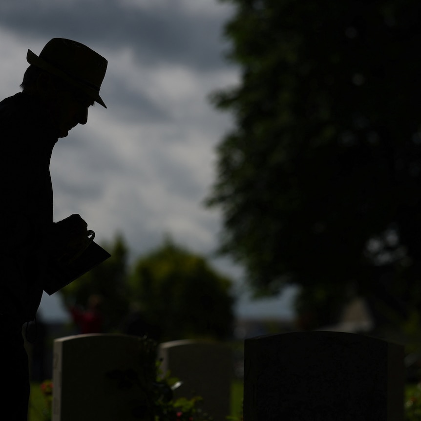 A silhouette of a man stands over a grave 