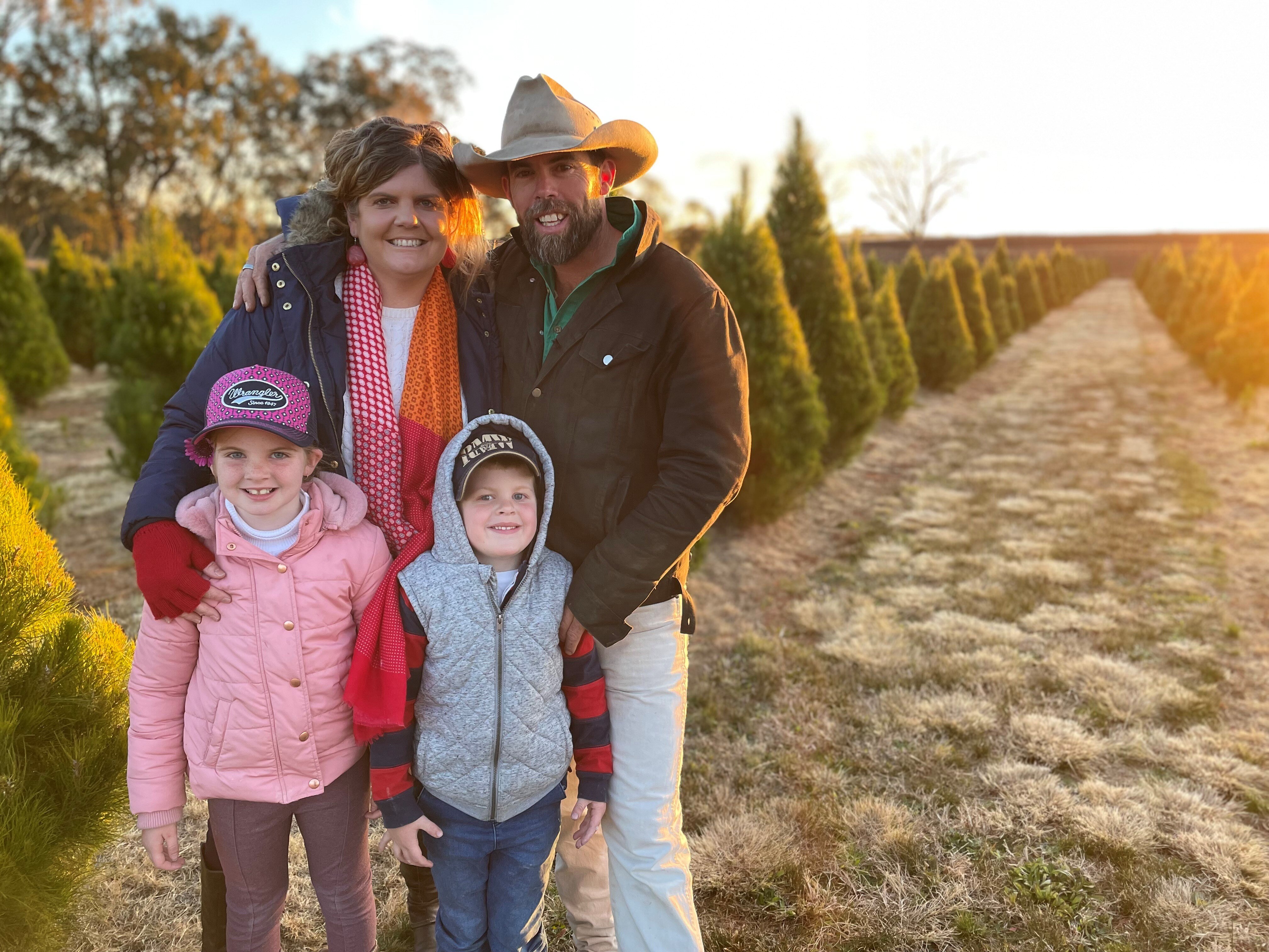Brad and Katrina Fraser and their children stand in front of rows of Christmas trees