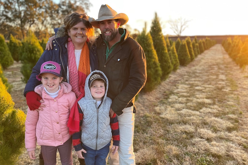 Brad and Katrina Fraser and their children stand in front of rows of Christmas trees