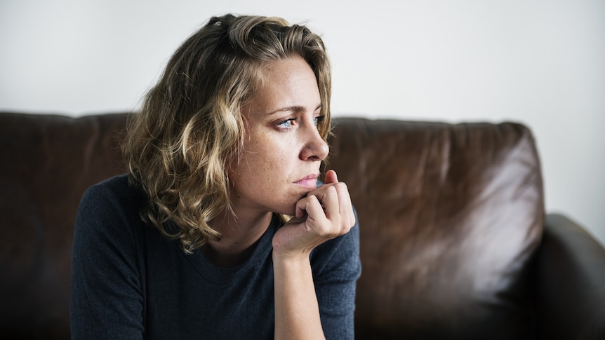 Woman sitting on a brown couch with her hand under chin looking upset