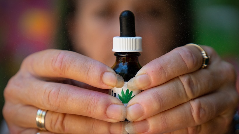 Two hands hold a small bottle with a dropper with a marijuana leaf on the label.