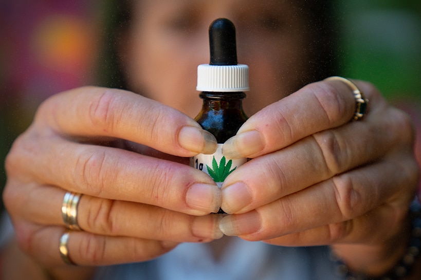 Two hands hold a small bottle with a dropper with a marijuana leaf on the label.