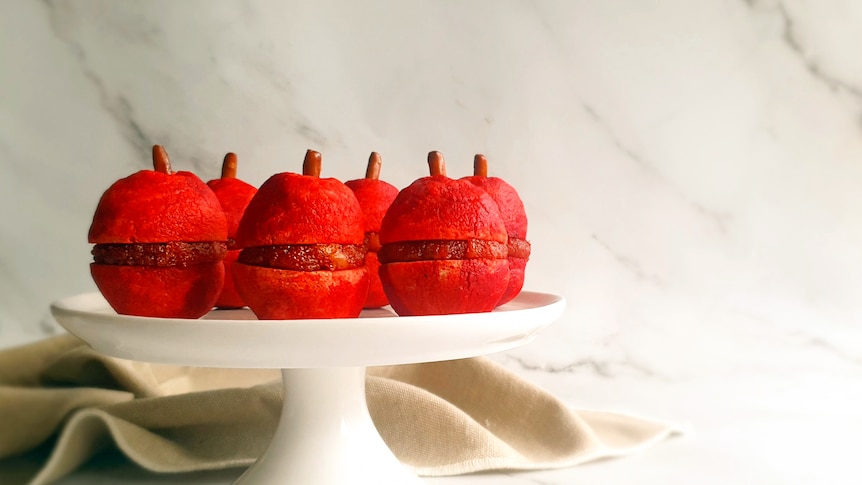 Red apple shaped melting moment biscuits with a pretzel stem, on a cake stand ready for a Rosh Hashana feast.