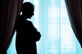 A woman stands at a window, arms folded.