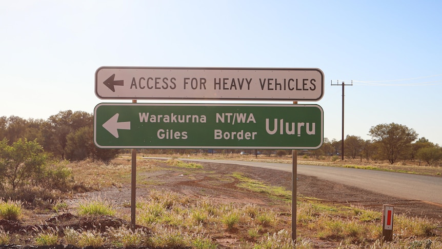A road sign pointing to Warakurna Giles, NT/WA Border, and Uluru