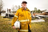 Peter Heward wearing a firefighting jacket holds a helmet with his name written on it.