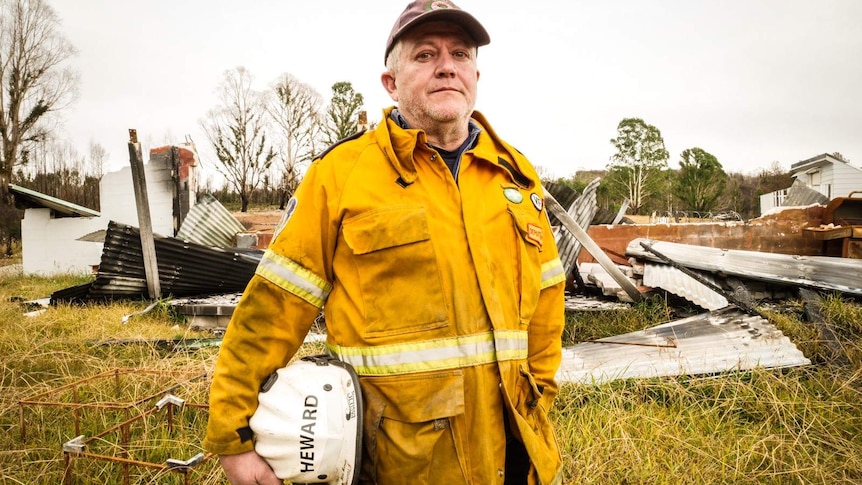 Peter Heward wearing a firefighting jacket holds a helmet with his name written on it.