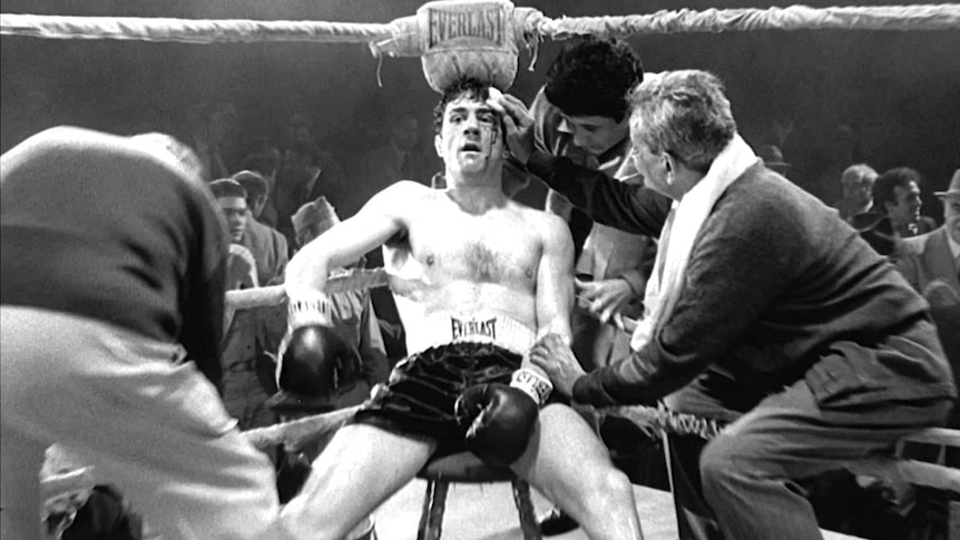Robert De Niro, playing Jake La Motta, leans against the corner of a boxing ring bleeding from the head.