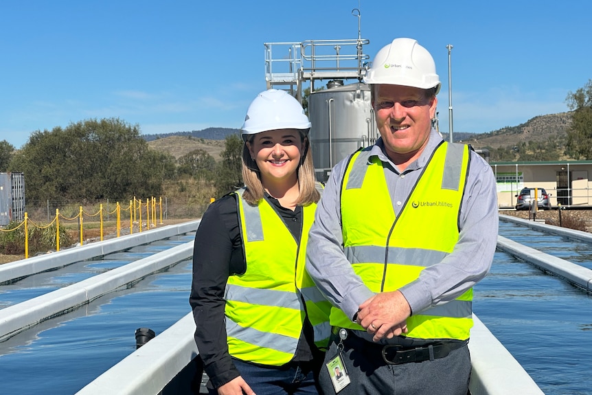 Two people stand in hard hats in front of a narrow pool