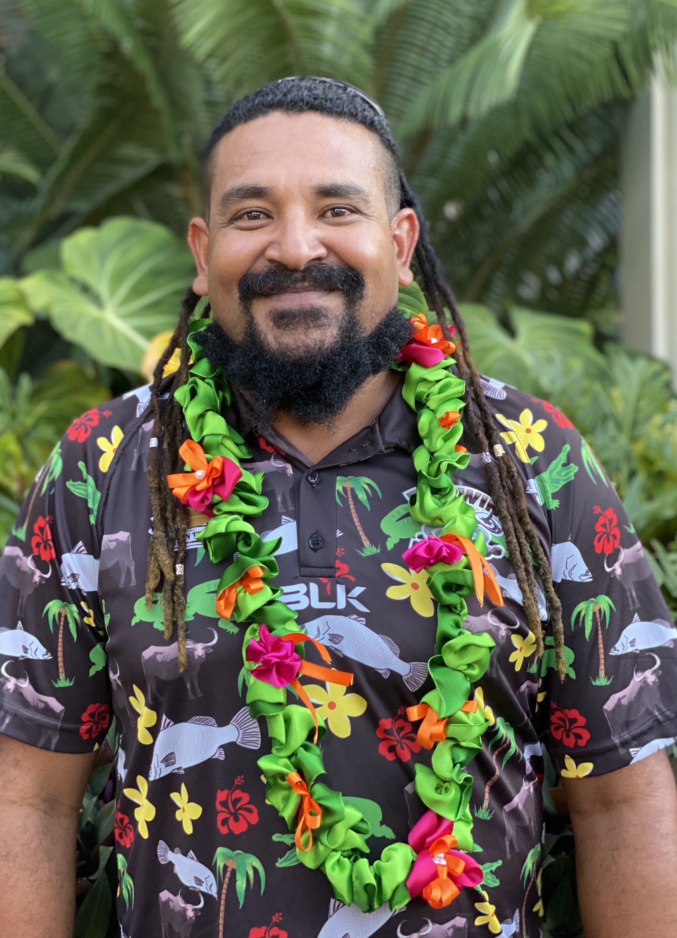 A Torres Strait Islander man wearing a colourful shirt and a lei smiles at the camera.