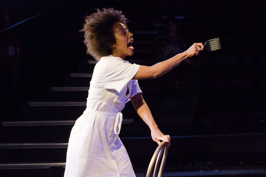 Production photograph of actor Ayeesha Ash during rehearsal of Brown Skin Girl, shouting across the stage with comb in hand.