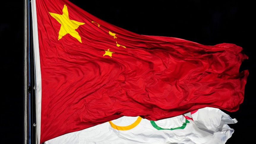 The Chinese flag waves in front of a flag with the Olympic rings on it.