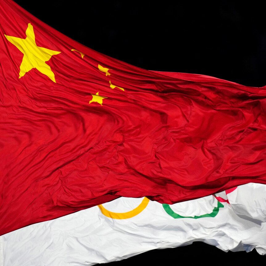 The Chinese flag waves in front of a flag with the Olympic rings on it.