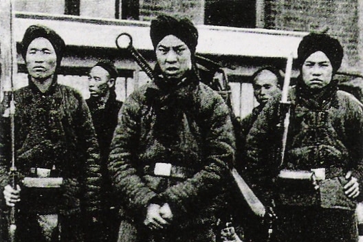 Black and white photo of men dressed in boots and winter clothing, standing with arms crossed, with serious expressions.