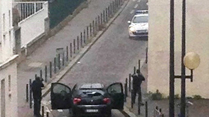 Armed gunmen face police officers near the offices of the French satirical newspaper Charlie Hebdo