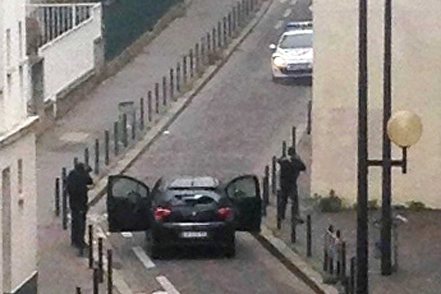 Armed gunmen face police officers near the offices of the French satirical newspaper Charlie Hebdo
