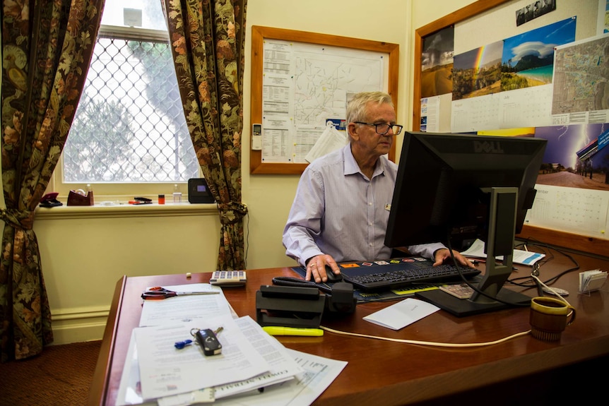 an older man with glasses sits behind a computer desk