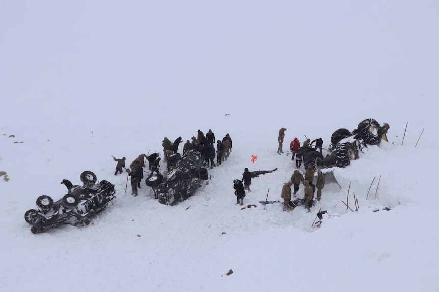 A view from above of about two dozen rescue workers in the snow near two overturned vehicles.