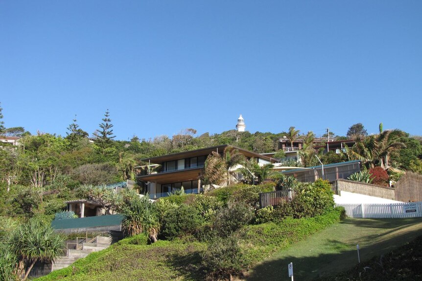 A large house is nestled on a green hill under a blue sky. 