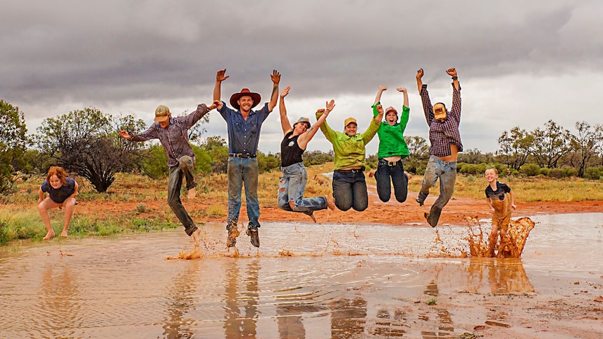 Adults and kids jump in air with puddle of water beneath them. 