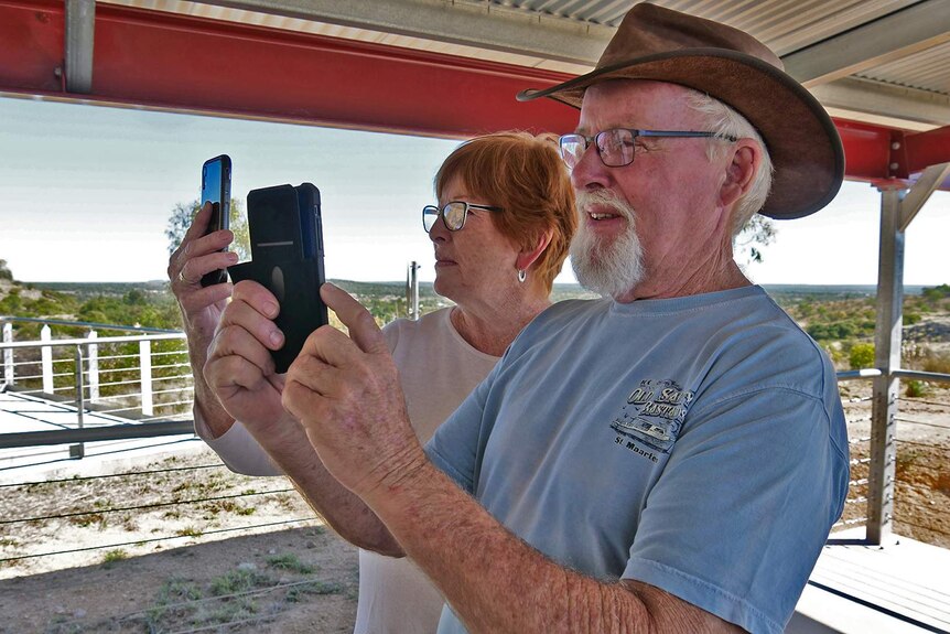 Two older people holding up their phones and looking at the screens