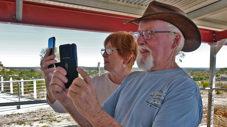 Two older people holding up their phones and looking at the screens