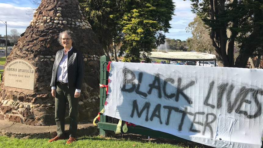 Cr Carolyn Crossley standing in front of a cairn in Sale, with a sign reading Black Lives Matter