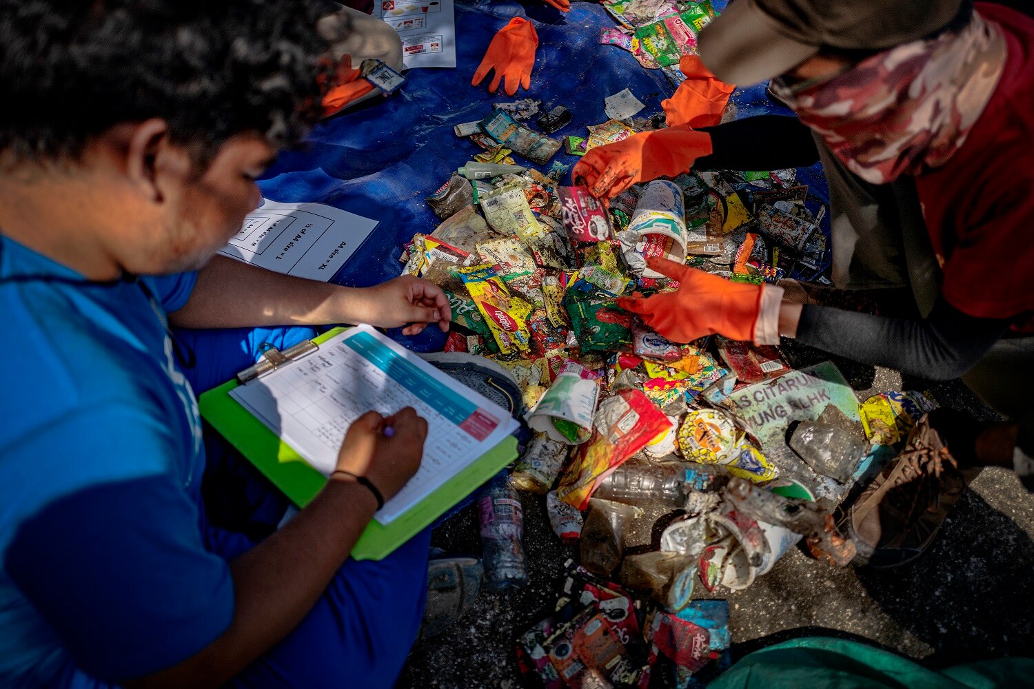 Man holding pen with paper in his lap, sitting in front of pile of rubbish.