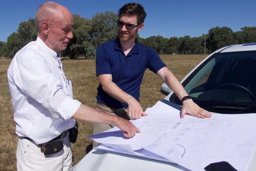 Two men look at a plan on the bonnet of a car.