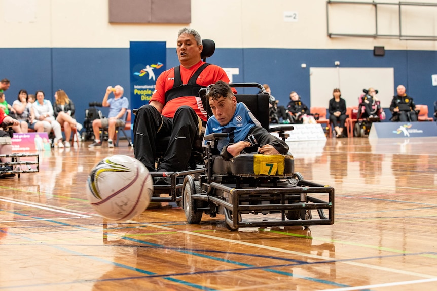 Two players chase a ball in their electric wheelchairs.