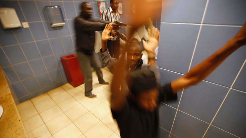 Armed police search customers taking cover inside a bathroom.