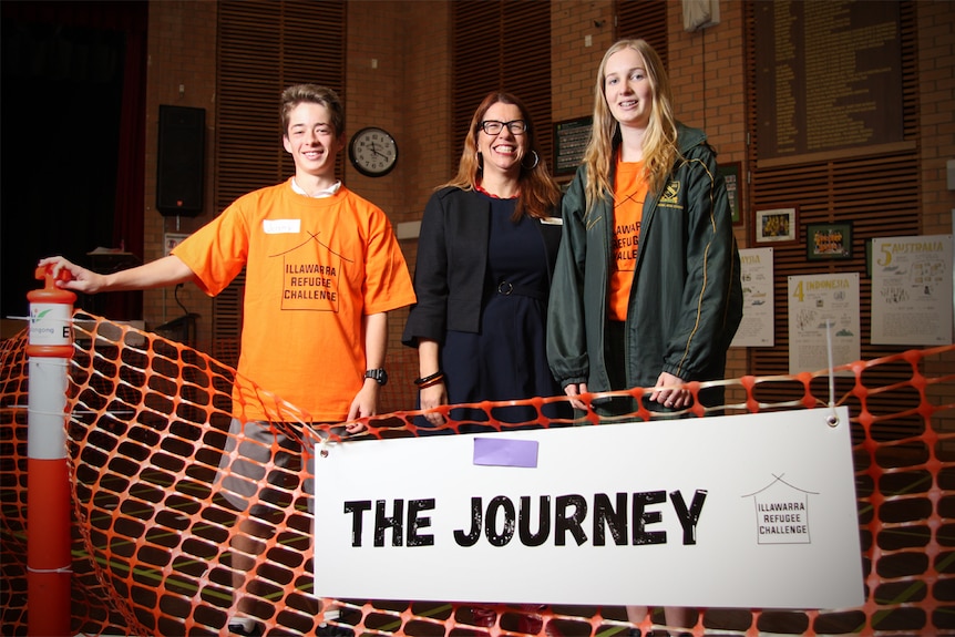 Jeremy Eager, Clare Matthews and Ruby Meiers stand in front on an orange fence sign that says 'the Journey'.