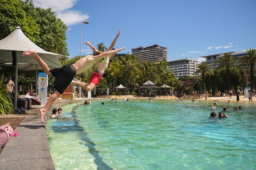 two boys captures in the middle of diving into a city pool with skycrapers in the background