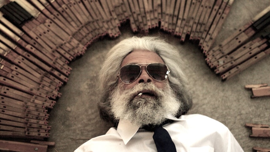 A bearded man wearing sunglasses lies on the floor surrounded by piano keys.