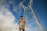 A woman looks up at a large transmission tower.
