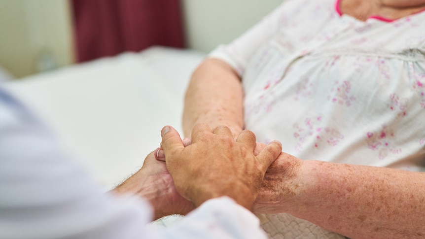 A woman in a hospital bed holding hands with another person.