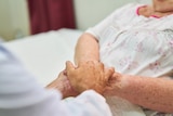 A woman in a hospital bed holding hands with another person.