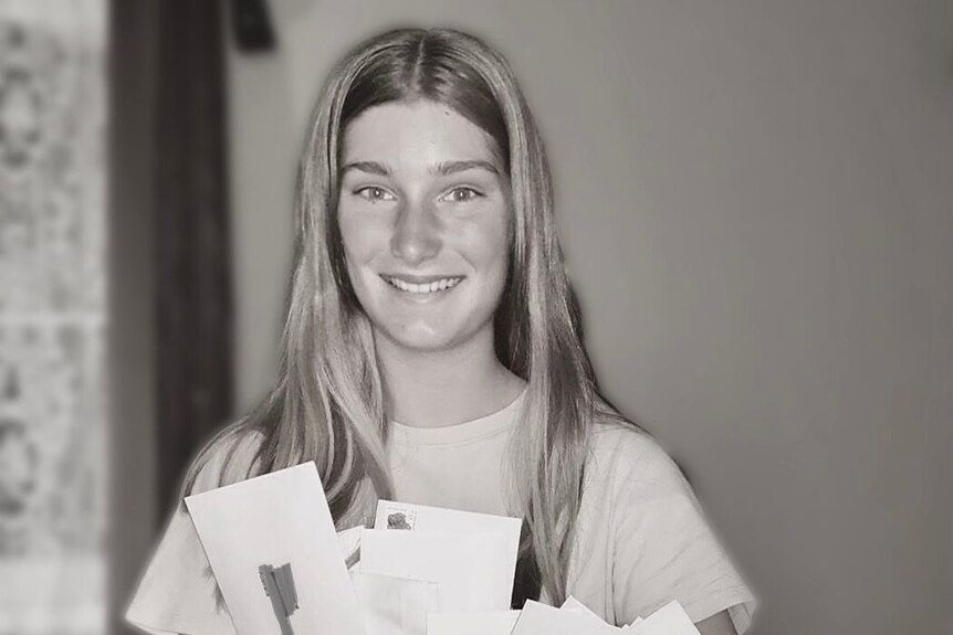 A teenage girl smiles holding a bundle of envelopes