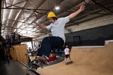 A skater slides his board across the top of an indoor half pipe