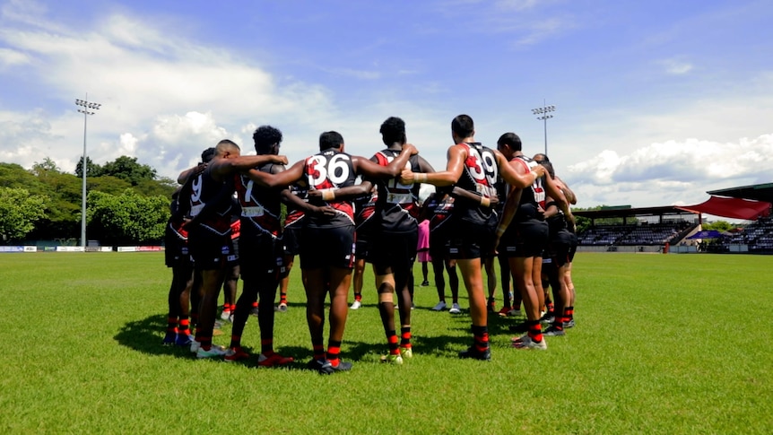 A group of male AFL players gather in a circle.