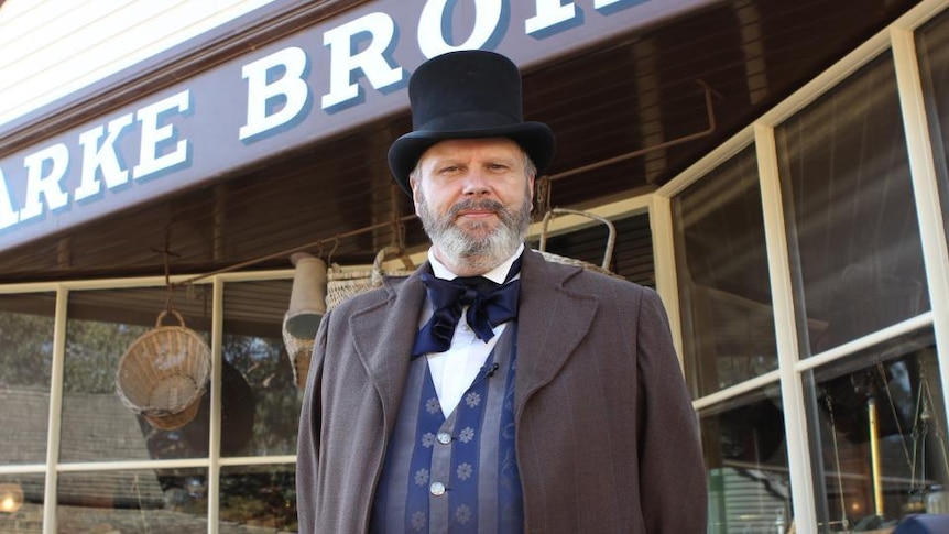 Man in top hat and coat stands in front of store