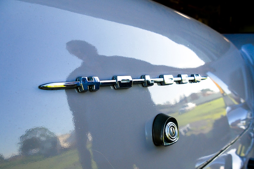 Close up of the chrome writing on Holden car, with silhouette of man