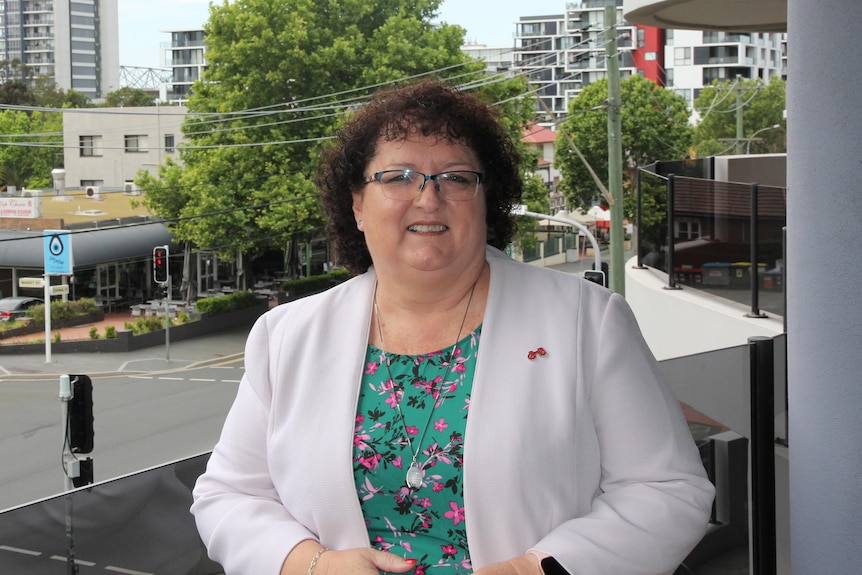 a woman in a white jacket and spectacles, smiling