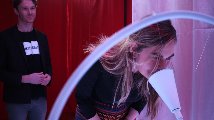 The Mix reporter Lisa Skerrett leans down and sniffs a while cone-shaped object as part of an exhibition.
